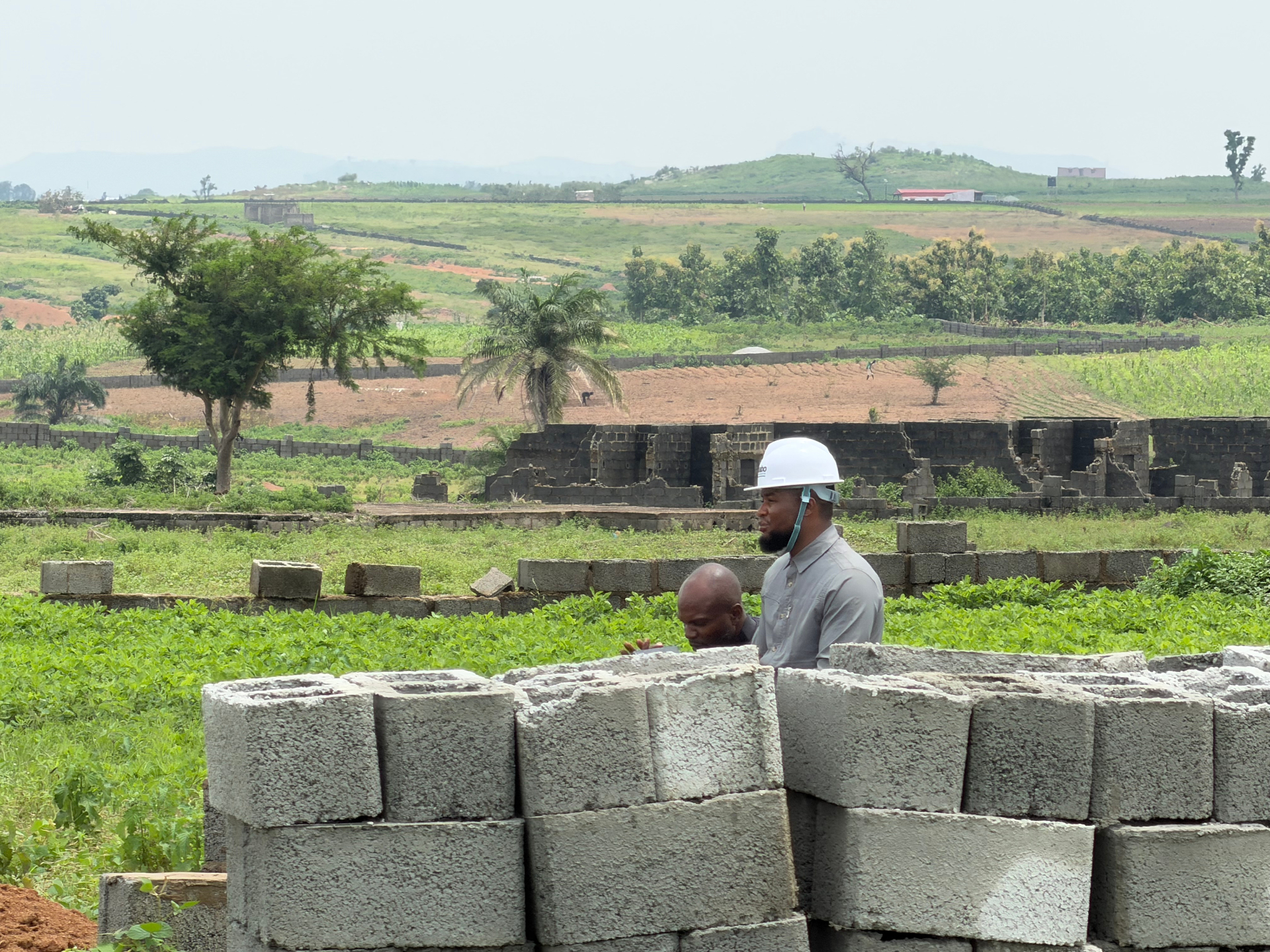 A Kaabo Investments staff member in a branded helmet with a builder beside stacked blocks on an estate under development
