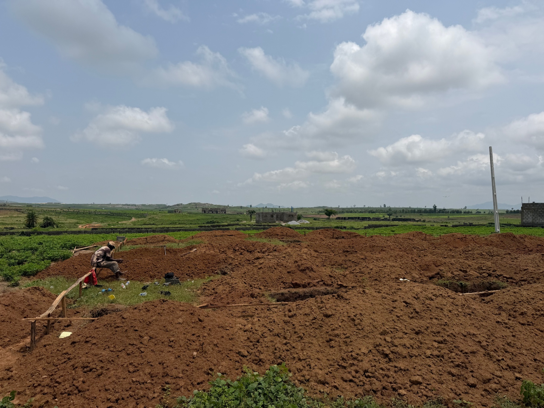 A worker setting out foundations on a cleared estate plot with the Abuja hills on the horizon