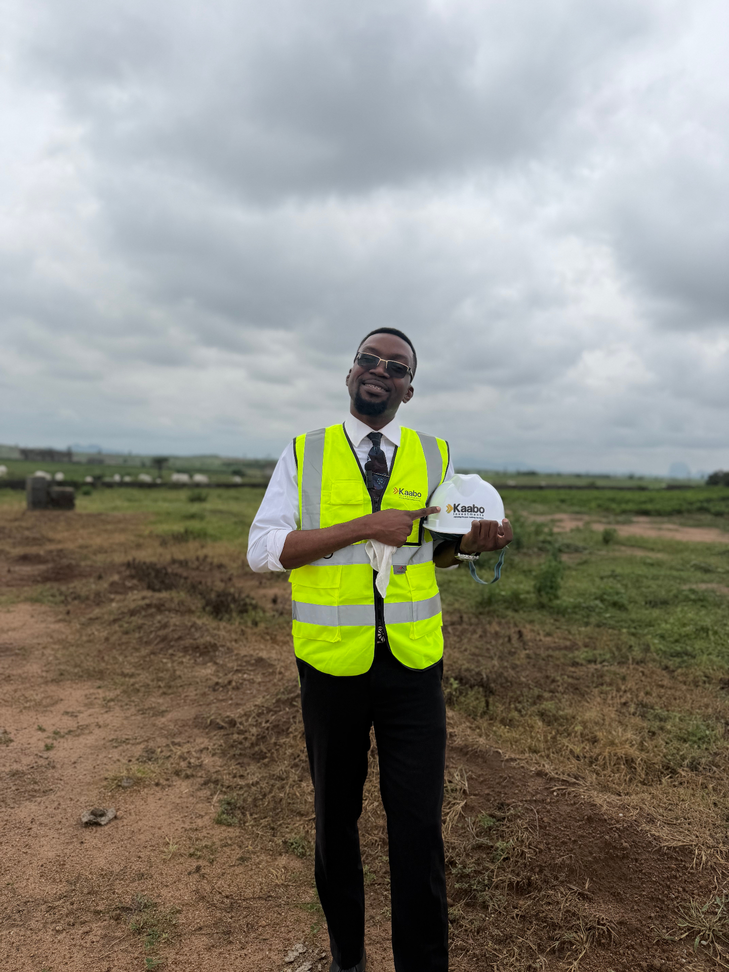 A Kaabo Investments staff member in branded hi-vis holding a Kaabo helmet on an estate plot outside Abuja